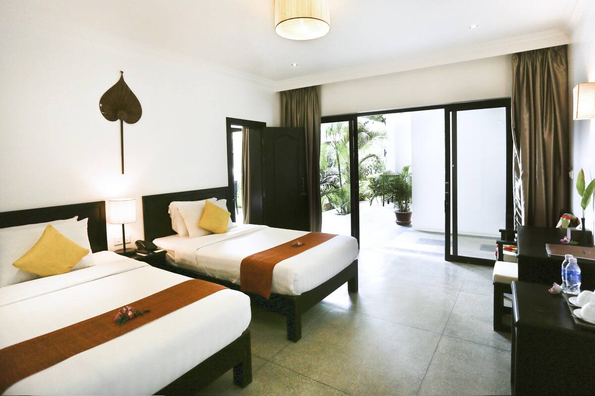 Een hotelkamer met twee bedden, een bureau, een lamp en uitzicht op de omgeving.