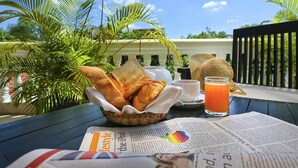 Une table avec un panier de croissants, une tasse de café, un verre de jus d’orange et un journal.