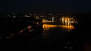 Une vue nocturne d’un pont dont les lumières se reflètent sur l’eau.