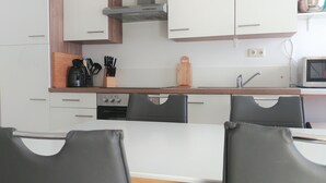 A modern kitchen with white cabinets, a stainless steel range hood, a microwave, and a sink. There are two black chairs at a table. - Apartment Möwennest Oberhof Boltenhagen (Oberhof)