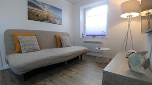 A modern living room with a sofa, a small side table, a floor lamp, and a decorative fish sculpture. - Apartment Möwennest Oberhof Boltenhagen (Oberhof)
