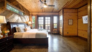 A spacious bedroom with a large bed, wooden ceiling, and a view through the window.