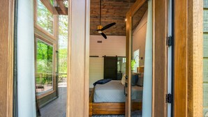 Un dormitorio con techo de madera, una cama, un ventilador de techo y vistas al exterior.