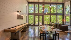 Una habitación amplia con un largo banco de madera, una mesa de comedor y un sofá. Amplias ventanas ofrecen vistas al exterior.