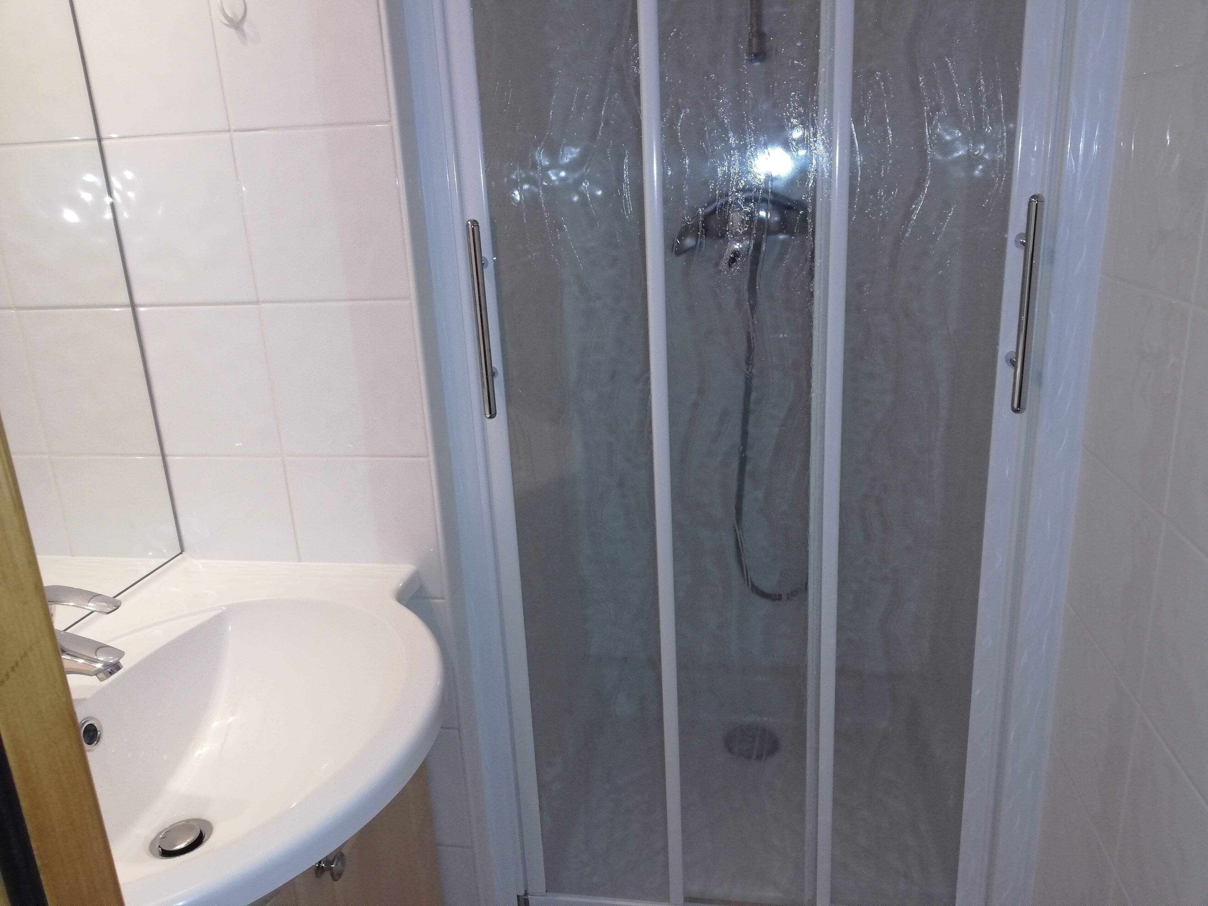 Une salle de bain avec un lavabo blanc, une douche en verre et des murs carrelés.