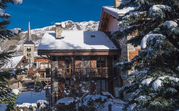 Um edifício em estilo chalé, com fachada de pedra, varandas de madeira e telhado coberto de neve.