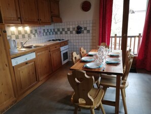 Cozinha com armários de madeira, painel de azulejos, fogão e mesa de jantar posta com pratos e copos.