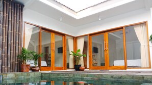 A poolside area with a clear view of a pool, wooden sliding doors, and potted plants. - Watukarung Prapto Homestay (Sendang)