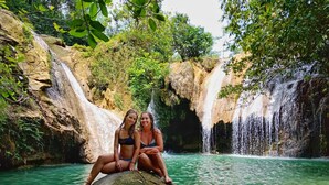 Two people sitting on a rock by a waterfall in a natural setting. - Watukarung Prapto Homestay (Sendang)
