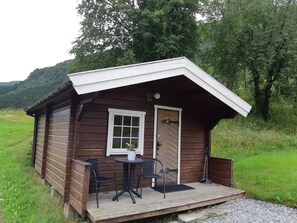 Una pequeña cabaña de madera con un porche, dos sillas y una mesa.