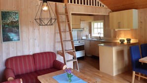 Interior de una cabaña de madera con cocina, comedor y un sofá rojo.