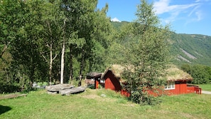 Een landelijke cottage met rieten dak, omgeven door weelderige begroeiing en bomen.
