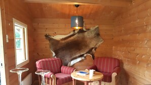 Interior acogedor de una cabaña con paredes de madera, una mesa de comedor, dos sillas tapizadas en rojo y un gran trozo de piel de animal colgado en la pared.