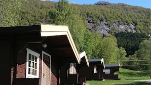 Un hilera de cabañas de madera con un patio cubierto de césped y montañas al fondo.