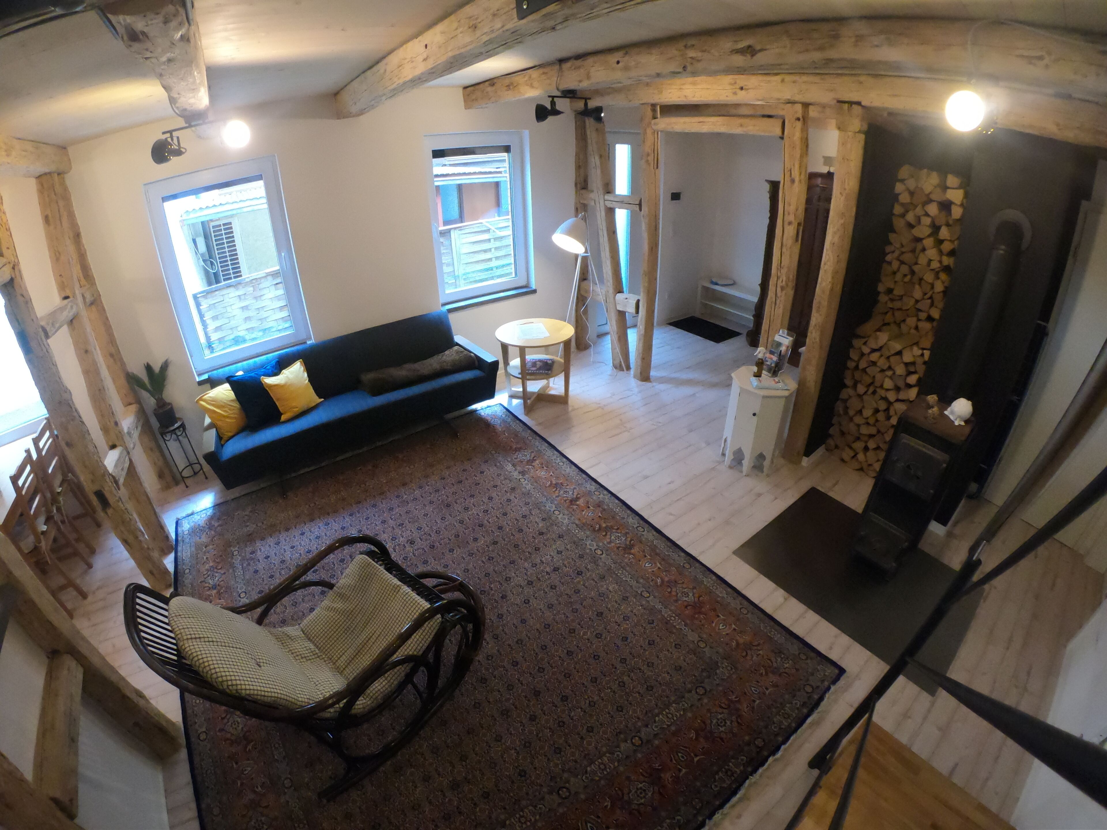 A cozy living room with a blue sofa, a rocking chair, a patterned rug, and a fireplace with wood storage.
