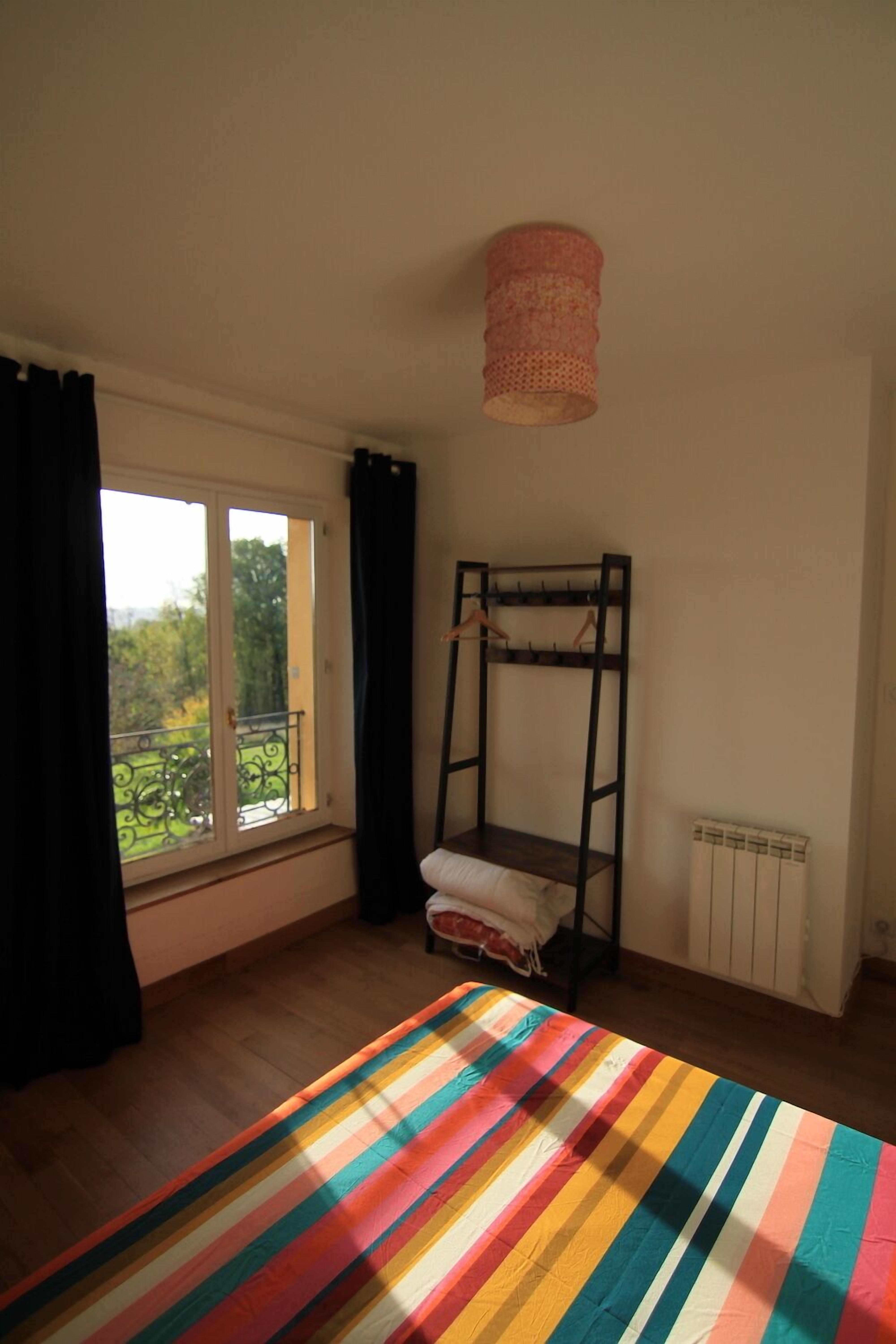 Une chambre avec un lit superposé, une fenêtre avec des rideaux, un radiateur et une couverture à rayures sur le lit.