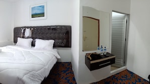 A hotel room with a large bed, a bedside table with a mirror, a window with curtains, and a wall-mounted TV. - Hotel Salma (Bukittinggi)