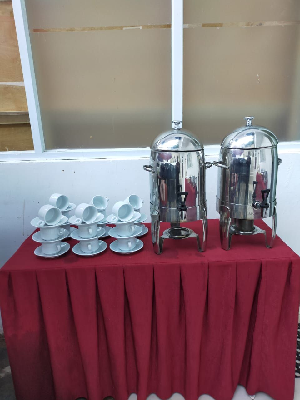 A table with two stainless steel coffee urns and multiple white teacups and saucers.