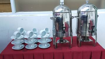Une table sur laquelle se trouvent deux thermos à café en acier inoxydable, ainsi que plusieurs tasses et soucoupes blanches.