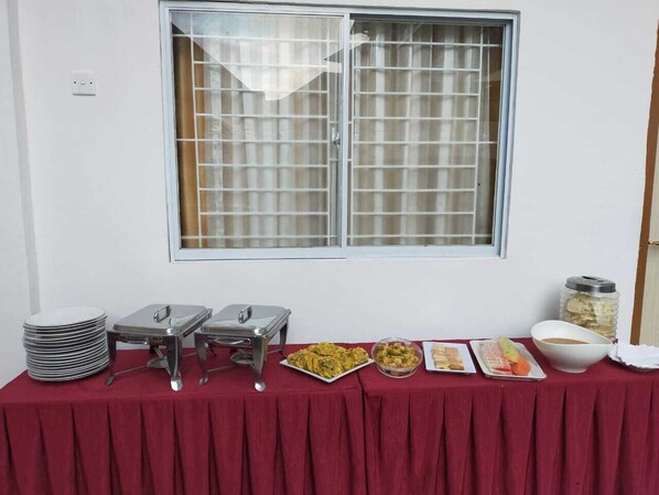 A buffet table with stacked plates, serving trays, and various food items.