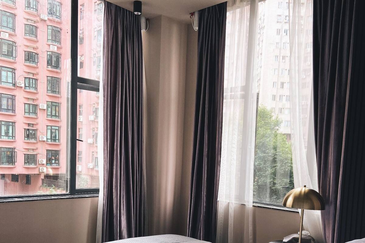Habitación de hotel con una cama grande, una mesita de noche con lámpara y una ventana con cortinas.