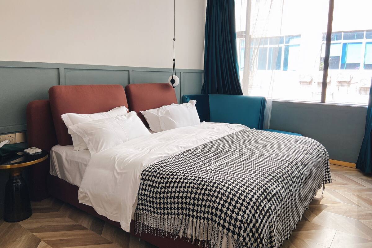 Habitación de hotel con cama, mesita de noche, ventana con cortinas y vistas al exterior.