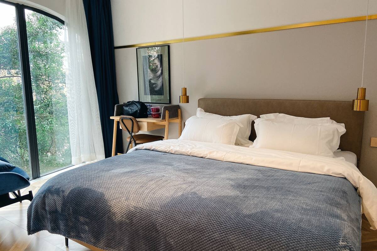 Una habitación de hotel con cama, escritorio, silla y ventana con cortinas.