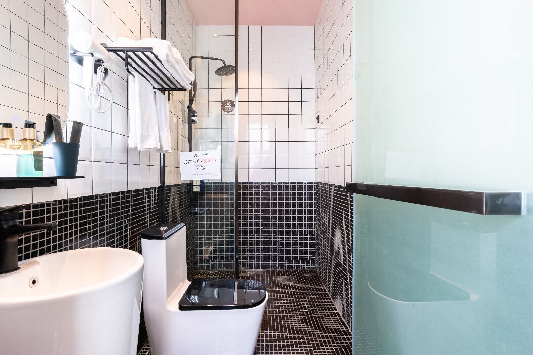A modern bathroom with a white sink, black and white tiled walls, a glass shower enclosure, and a black bathtub.