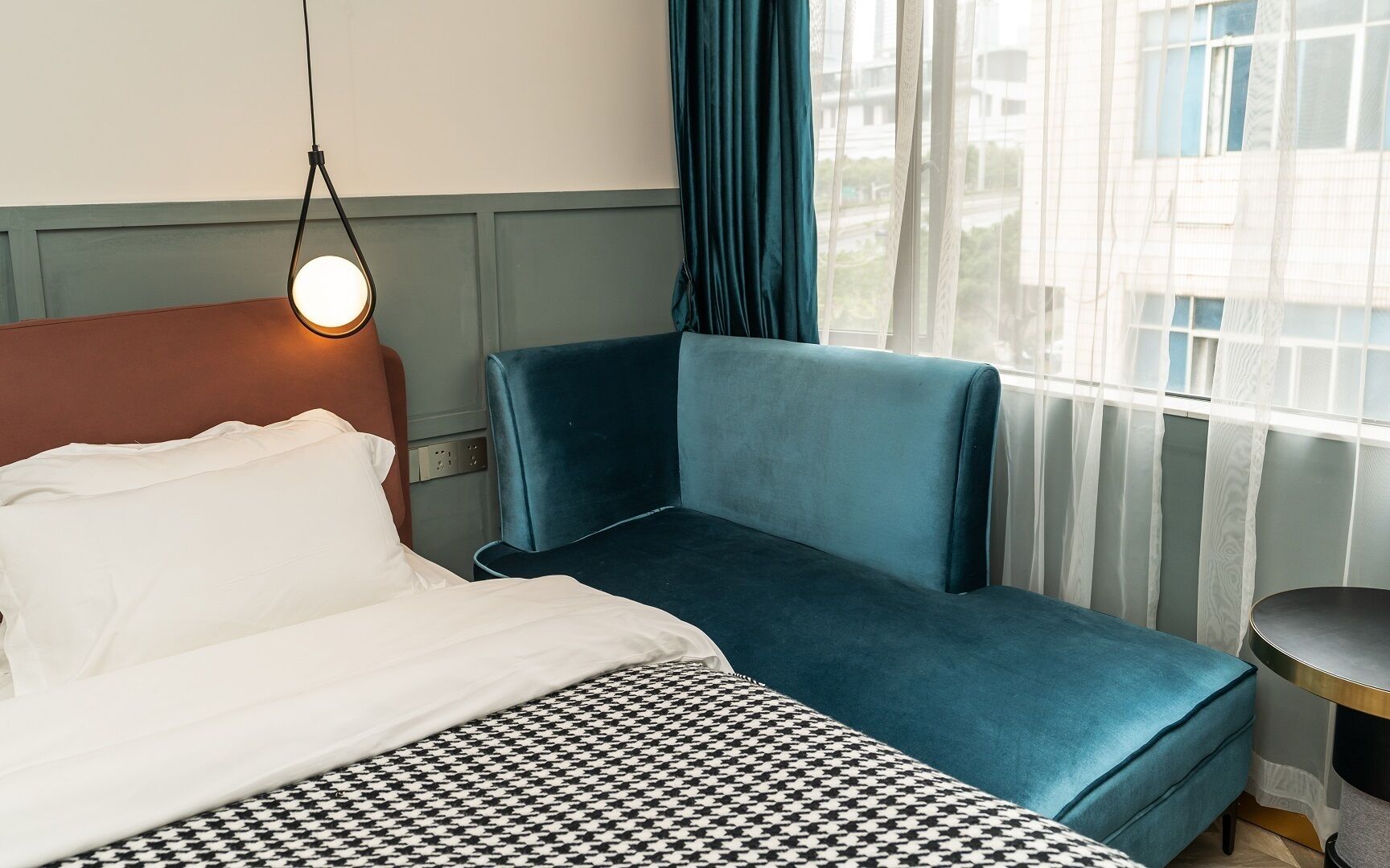Ett hotellrum med en säng, en blå soffa, ett litet bord och ett fönster med gardiner.