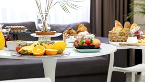 Une table dressée pour le petit-déjeuner, avec une variété d’aliments, notamment des fruits, des viennoiseries et un vase contenant des plantes séchées.