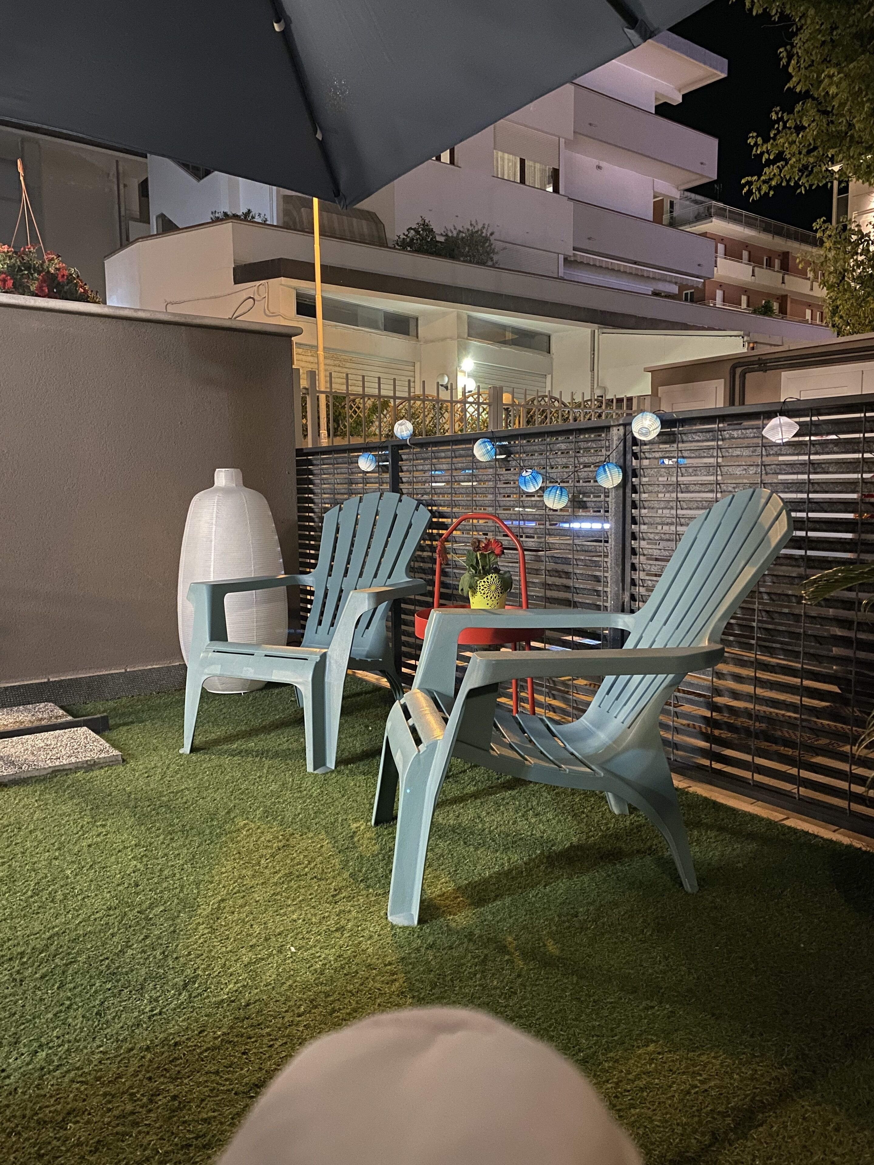 An outdoor seating area with two blue chairs and a table, a white cooler, and a decorative plant.
