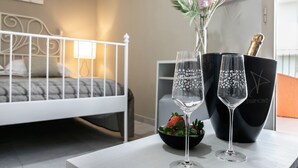 Une chambre d’hôtel avec un lit, une table sur laquelle sont posés deux coupes à champagne et un saladier de fruits, ainsi qu’un seau noir contenant une bouteille.