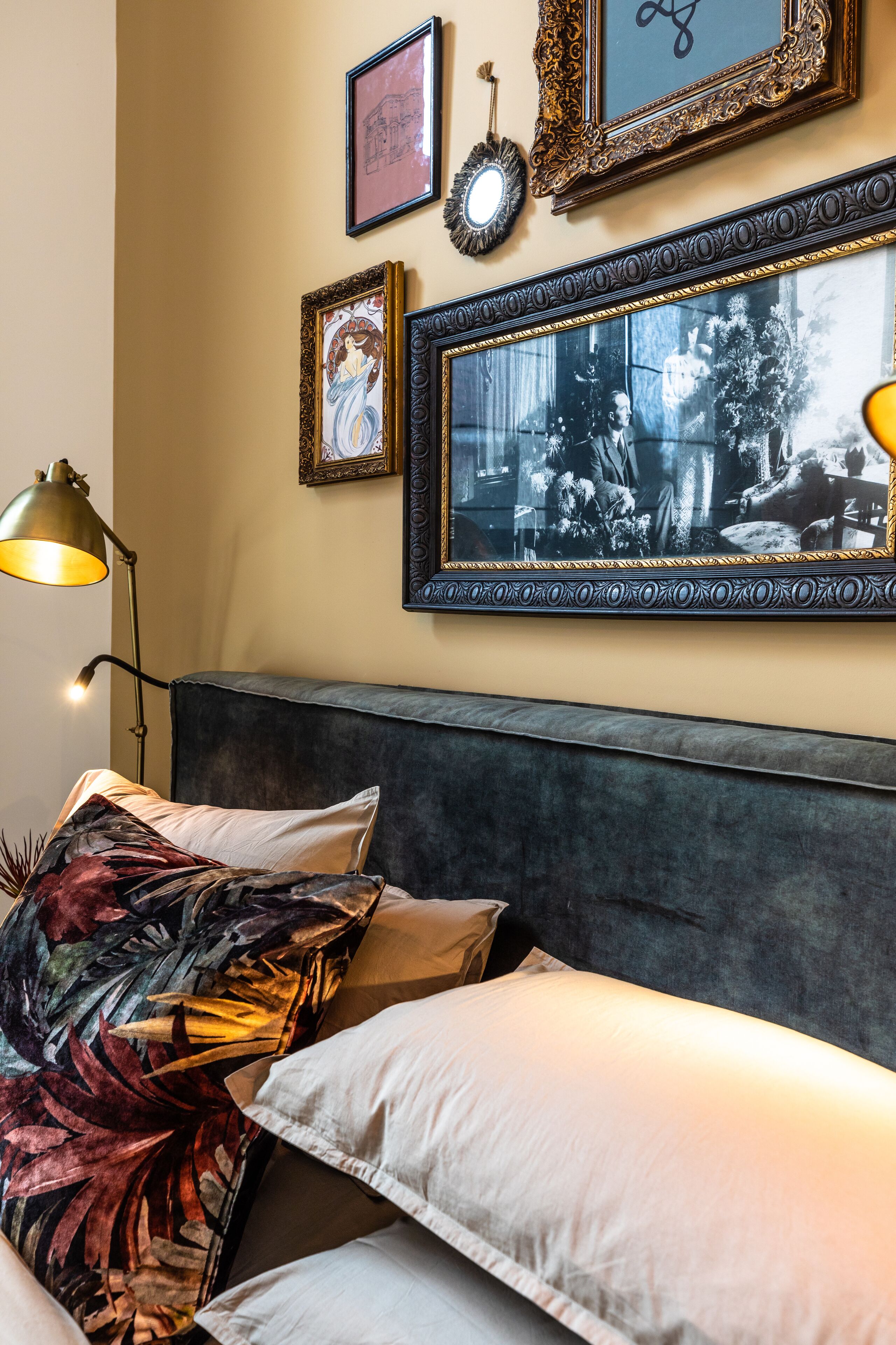 Een slaapkamer met een bed, kussens, een hoofdbord en ingelijste foto's aan de muur.