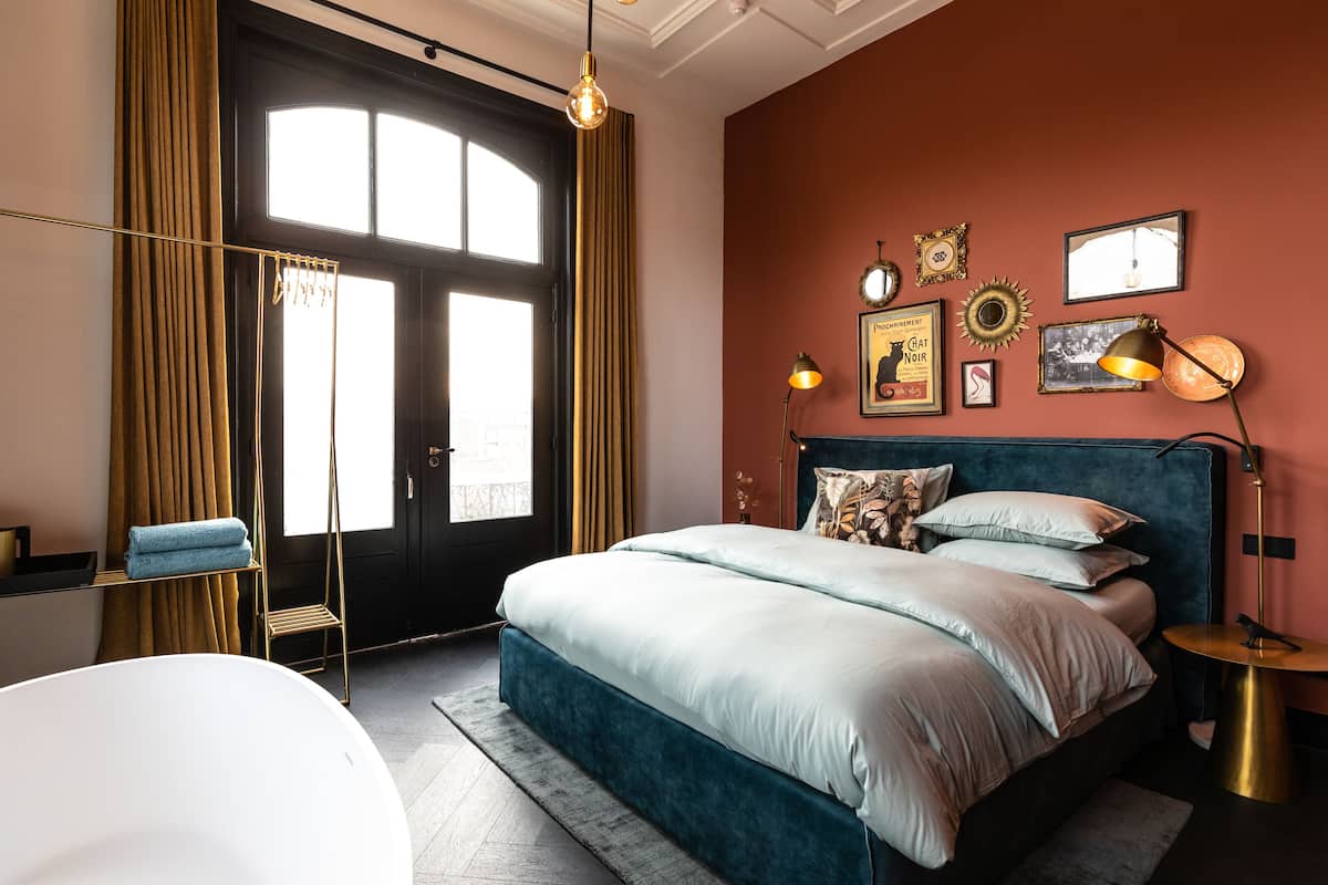 A bedroom with a large bed, a desk, a chair, and a window with curtains.