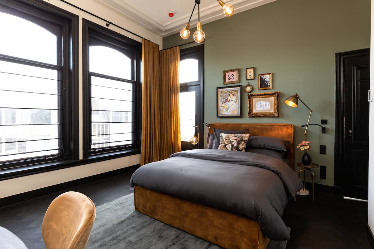 A modern bedroom with a large bed, a wooden headboard, and a view of the city through large windows.