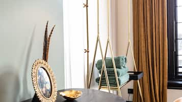 Une pièce moderne avec une table ronde de couleur sombre, un miroir décoratif, un livre intitulé « META MORPH OSE », une lampe sur pied et une fenêtre avec des rideaux.