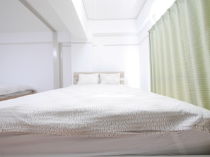 Una cama bien hecha con una colcha estampada en una habitación luminosa con tragaluz y cortina verde.
