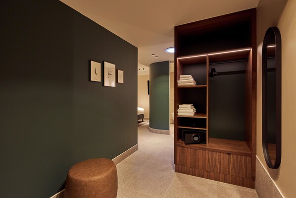 A hallway with a wooden closet, a round stool, and framed pictures on the wall.