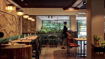 A modern restaurant interior with green booths, wooden tables, and hanging pendant lights.