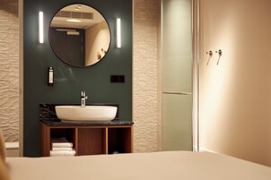 A modern bathroom with a round mirror, a white sink, and a wooden vanity.