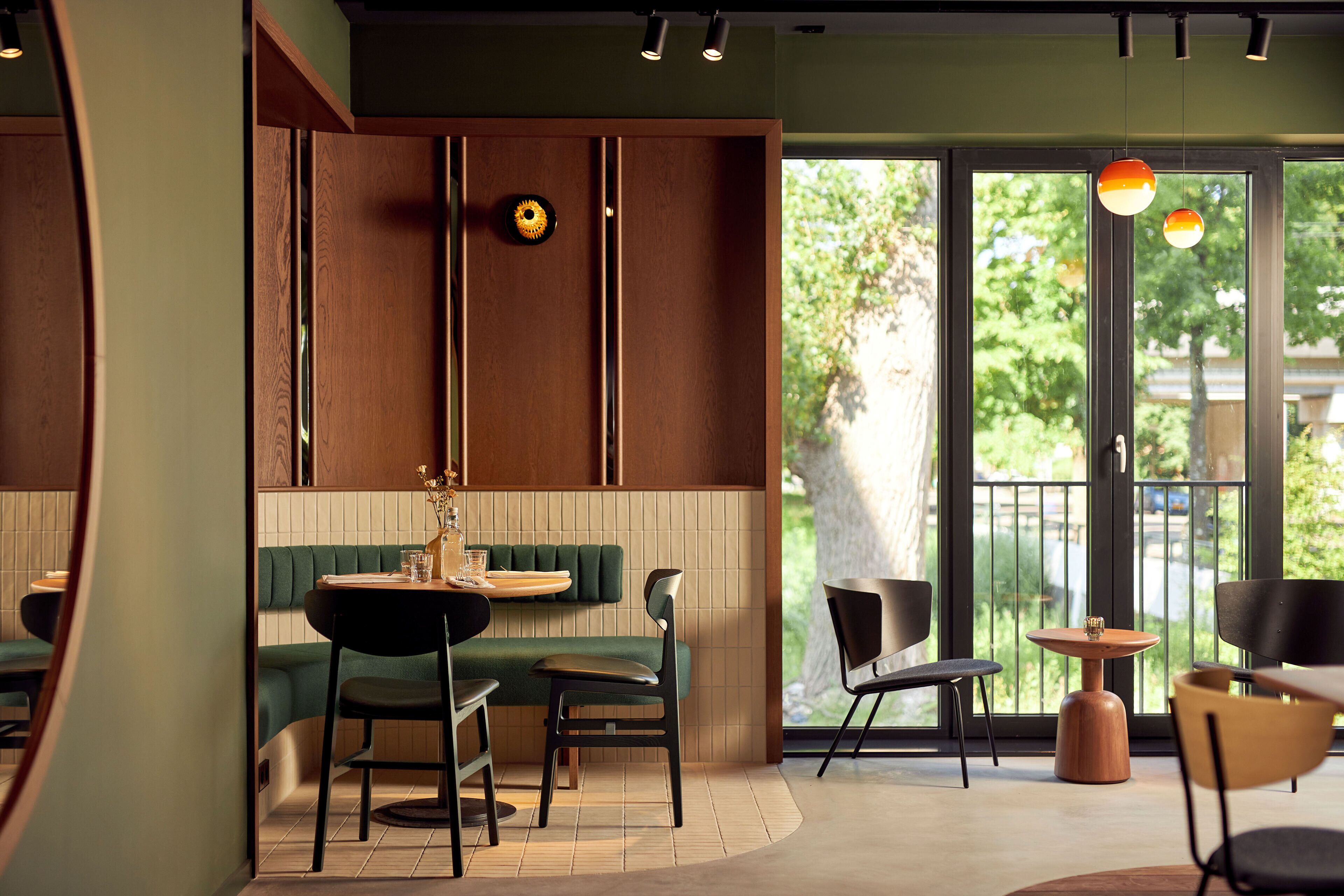 Interior de restaurante con zona de cabinas, una mesa pequeña con sillas y vista a áreas verdes exteriores.