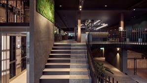 A modern interior with a staircase leading to an upper level, a glass elevator, and a green wall. - Met Hotel Amsterdam (Amsterdam)