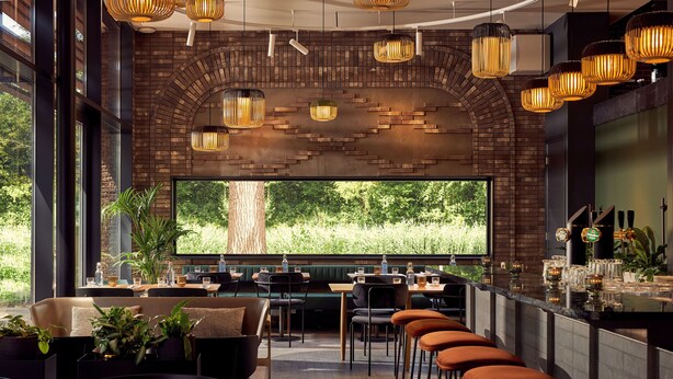 A modern restaurant with a brick wall, large windows, and a bar area with stools. - Met Hotel Amsterdam (Amsterdam)