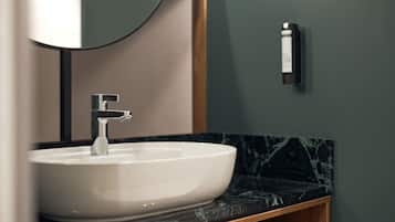 A modern bathroom with a white sink, a round mirror, and a black soap dispenser on the wall.