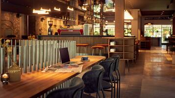 Zona de bar moderna amb un llarg mostrador de fusta, diversos tamborets i diferents opcions d'asseients, incloent tamborets alts i un bar amb una màquina de cafè.