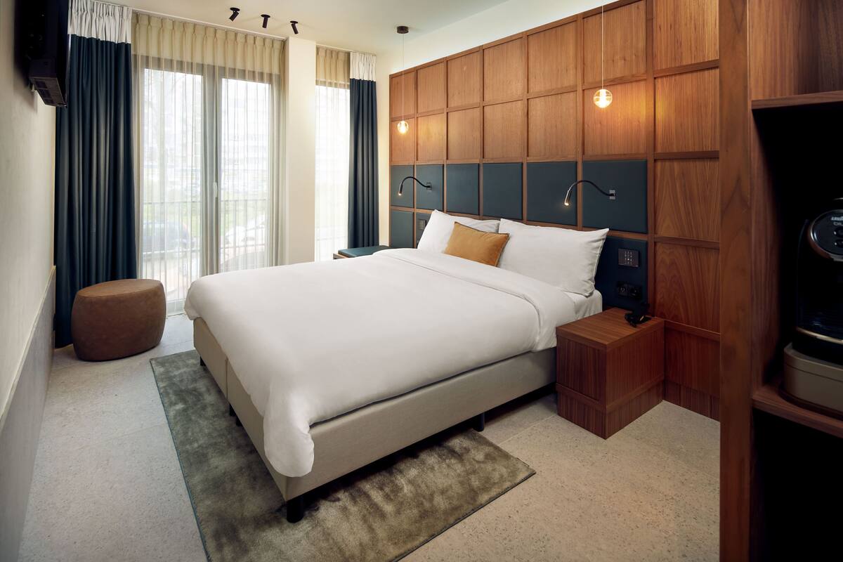 A modern hotel room with a large bed, wooden headboard, bedside tables, and a TV.