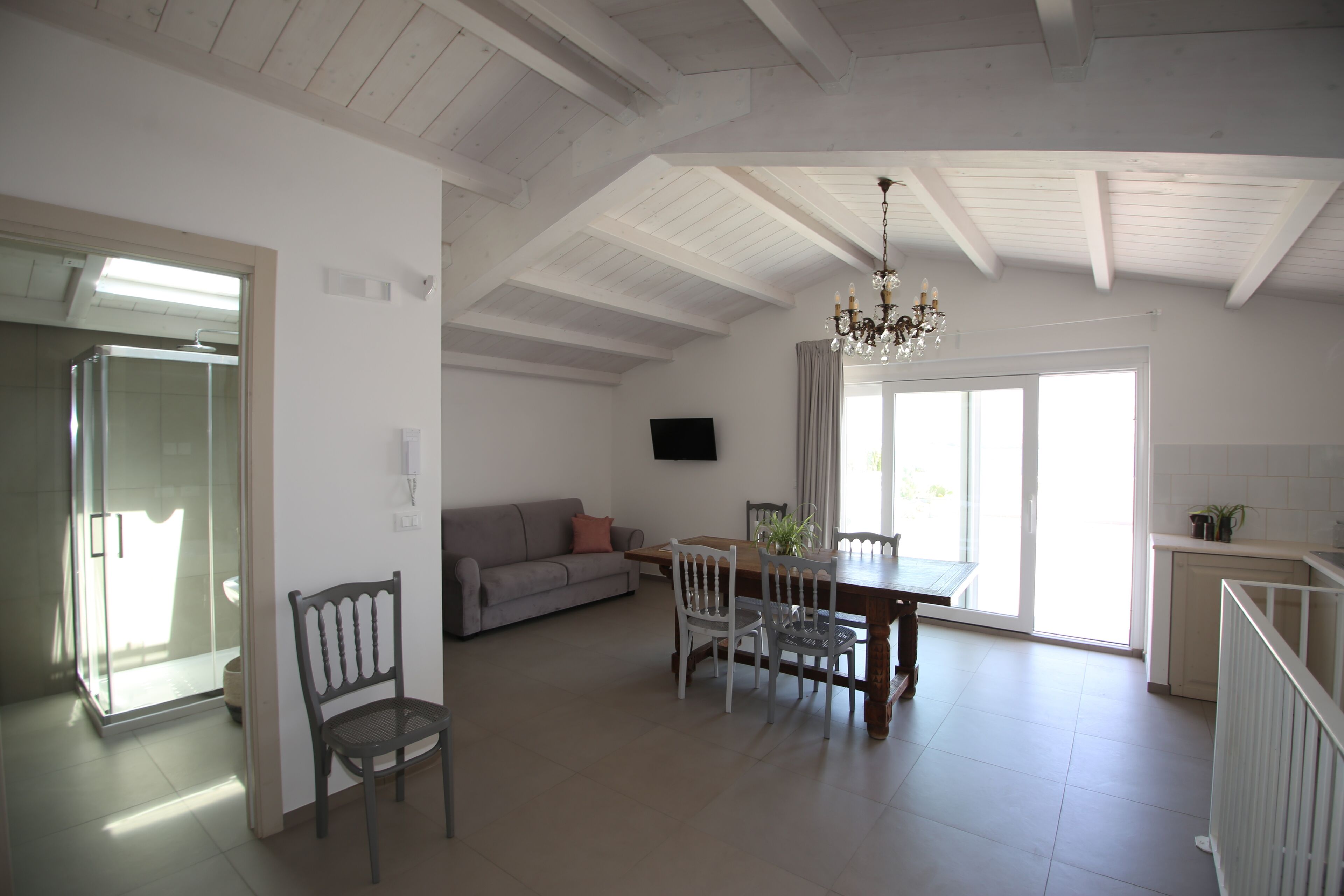 A spacious living area with a dining table, chairs, a sofa, and a chandelier.
