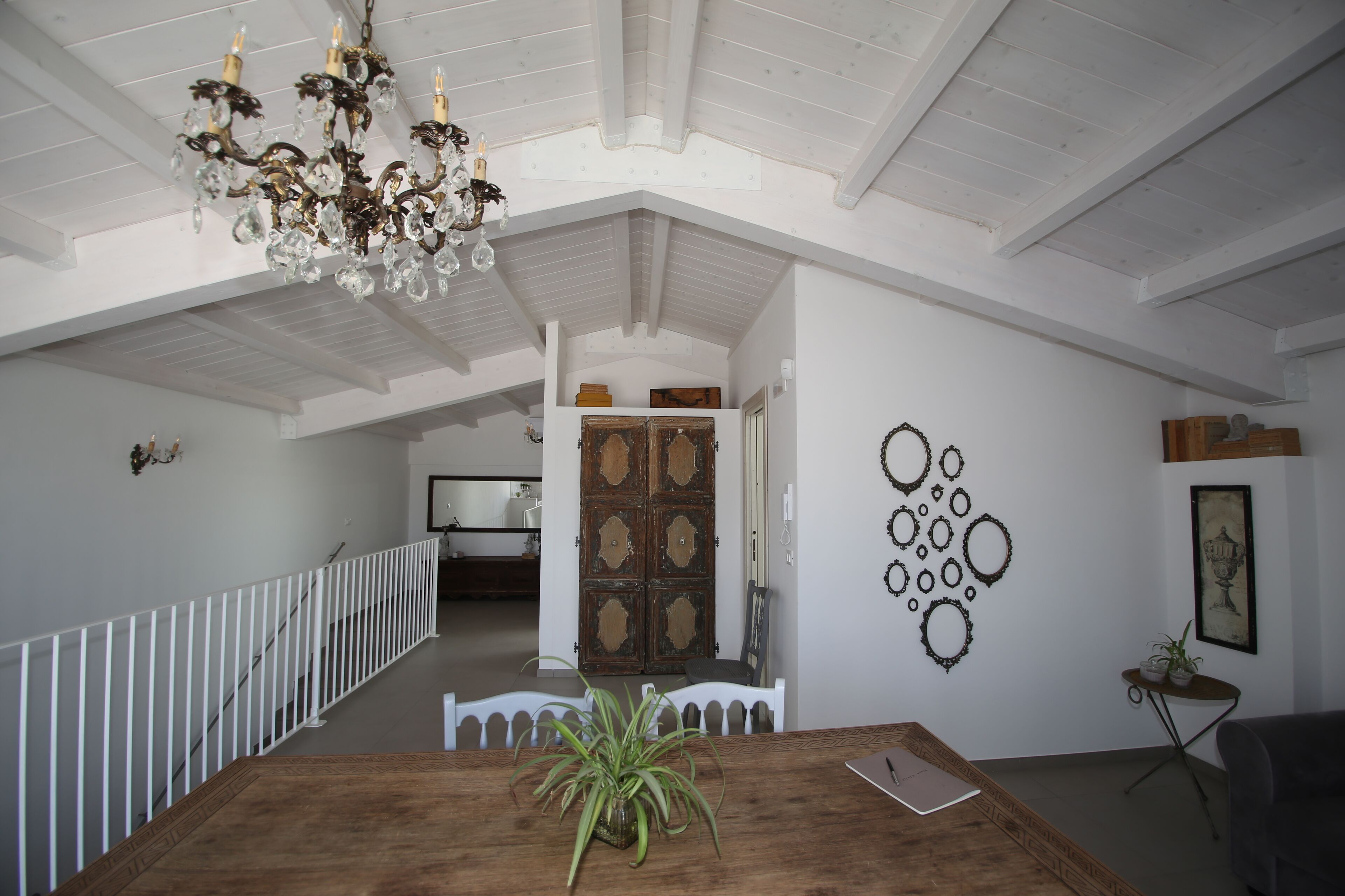 Une pièce spacieuse avec une table à manger en bois, un lustre, une balustrade blanche et un escalier menant à un autre espace.