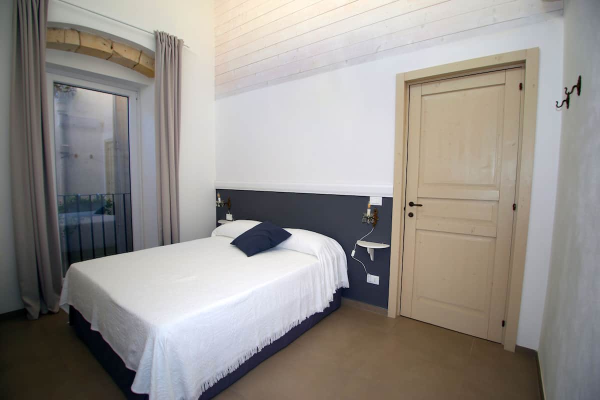 A bedroom with a bed, a door, and a window with curtains.