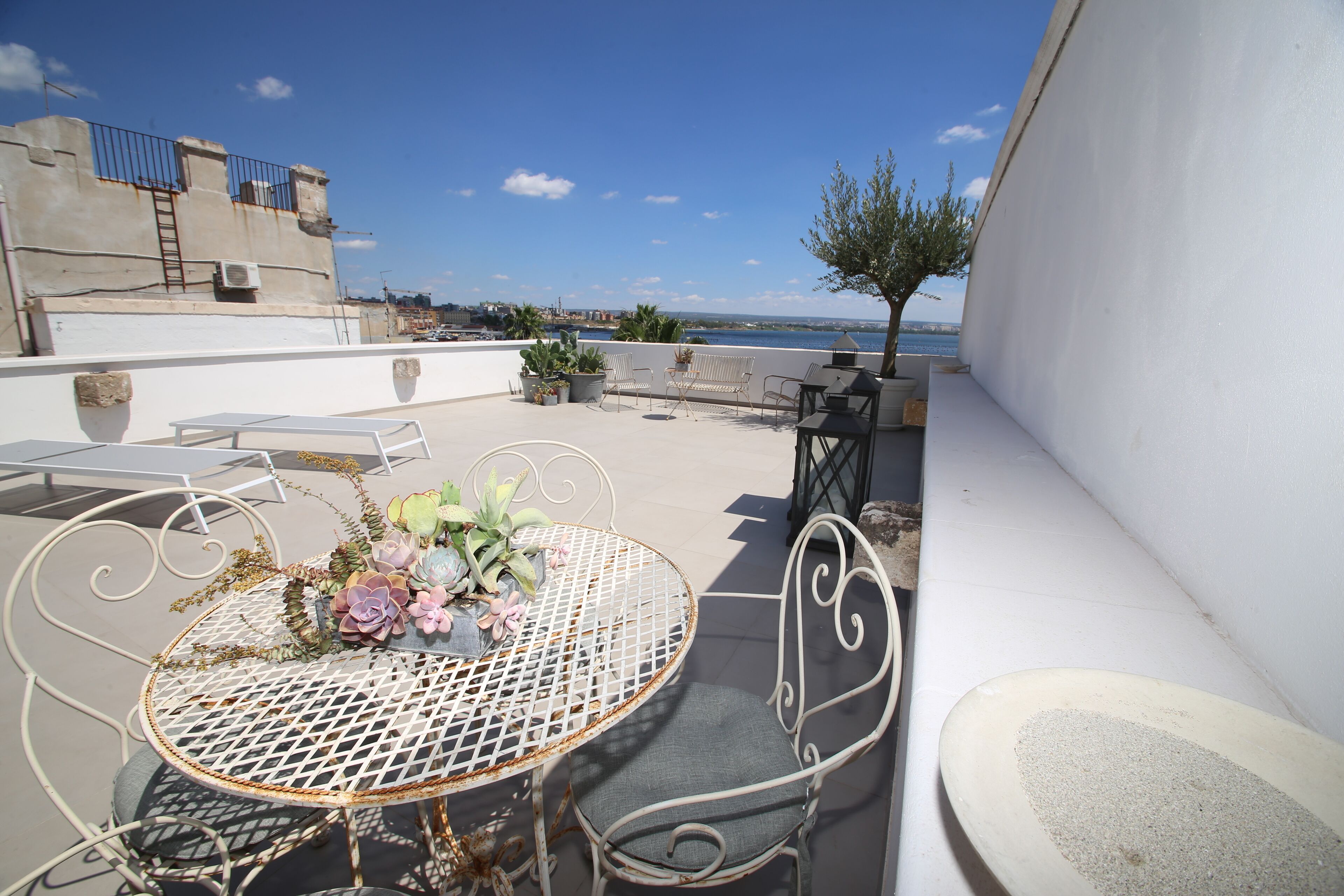 Une terrasse sur le toit avec une table ronde en métal, deux chaises et un petit arbre.